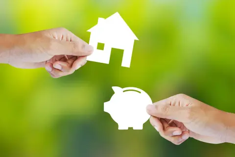 Manos intercambian una casa y una alcancía, simbolizando la decisión de alquilar o comprar.