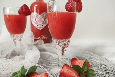 Dwa kieliszki z orzeźwiającym, czerwonym drinkiem, ozdobione truskawkami. Obok butelka z napisem "Sweet Heart", sugerująca pyszny alkohol truskawkowy.
