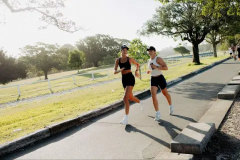 Deux femmes profitent d'un entraînement de course à pied matinal dans un parc verdoyant, leurs sourires reflétant leur plaisir.