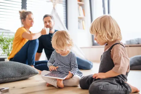 Rozpieszczone dziecko pochłonięte tabletem, podczas gdy rodzice w tle piją kawę.