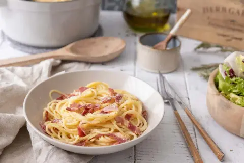 Un plat de spaghetti crémeux, garni de lardons croustillants, évoque la vraie recette carbonara italienne. Une salade fraîche accompagne ce délice.