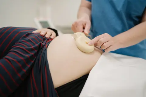 Une main ajuste un moniteur sur le ventre d'une femme enceinte. Apprendre à comment lire un monitoring est essentiel pour le suivi de grossesse.