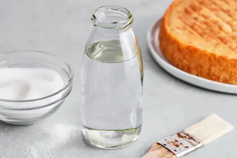 Zutaten für zuckersirup selber machen: Zucker, Wasser in Flasche, Pinsel und ein Kuchenboden.