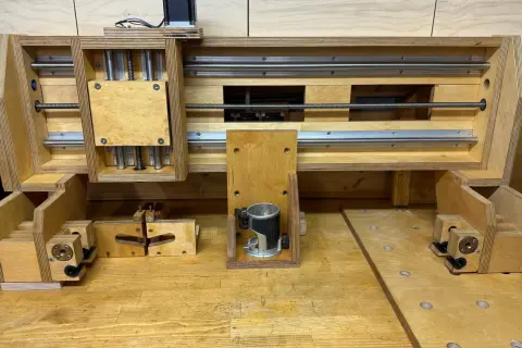 Domowa frezarka CNC DIY z drewna i metalowych prowadnic. Widać silnik krokowy, wrzeciono z frezarką ręczną i mechanizm śrubowy.