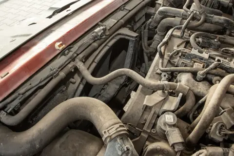 Wnętrze silnika samochodu, pełne przewodów i rurek. Widać fragmenty metalowe i plastikowe, a także kurz. W tle wentylator.
