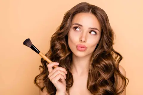 Ragazza con pennello da trucco, pensierosa, mentre impara a truccarsi.