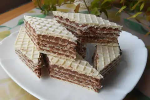Trójkątne wafle przełożone kremem z mleka w proszku, ułożone na białym talerzu.