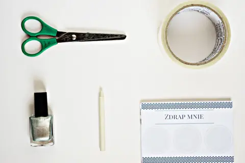 Potrzebne do zrobienia zdrapki DIY: nożyczki, srebrny lakier, taśma, biała kredka i kartka z napisem "ZDRAP MNIE".
