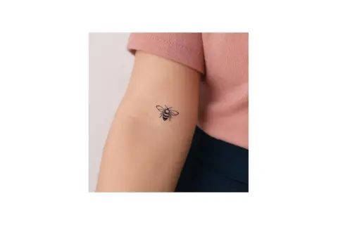 Un delicado tatuaje abeja minimalista adorna el brazo de una persona, un pequeño símbolo de trabajo y dulzura.