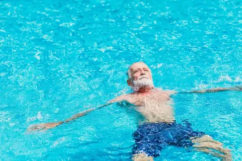 Ein älterer Mann mit Bart entspannt sich im Wasser. Schwimmen bei Arthrose kann Linderung verschaffen.