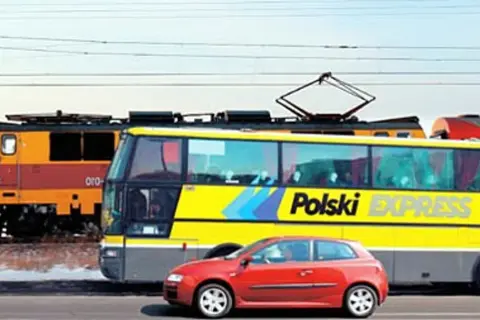 Pociąg, żółty autobus "Polski Express" i czerwony samochód jadą obok siebie, jakby na trasie katowice-kraków.