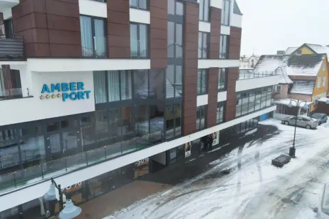 Nowoczesny hotel Amber Port w zimowej scenerii. Na fasadzie widoczny napis "AMBER PORT" i gwiazdki. Ulica pokryta śniegiem.