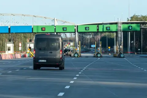 Czarny van zbliża się do bramek autostradowych z zielonymi znakami kierunkowymi.