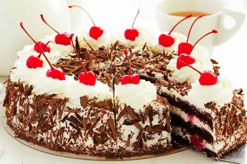Una deliziosa foresta nera torta, ricoperta di panna montata e ciliegie rosse, con scaglie di cioccolato che la rendono irresistibile.