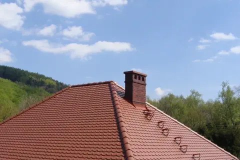 Solidna cegła klinkierowa na komin, dumnie wznosząca się nad czerwonym dachem.