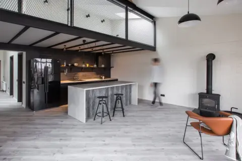 Nowoczesna kuchnia z wyspą i antresolą. Inspiracje dla loftowych wnętrz, gdzie industrialny styl łączy się z przytulnością kominka i wygodnym fotelem.