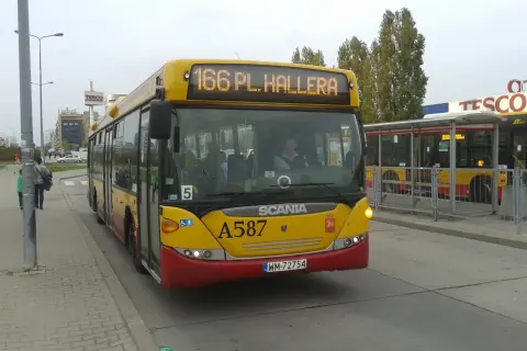 Żółty autobus linii 166 w Warszawie, z napisem "166 PL. HALLERA" na wyświetlaczu, stoi na przystanku obok centrum handlowego Tesco.