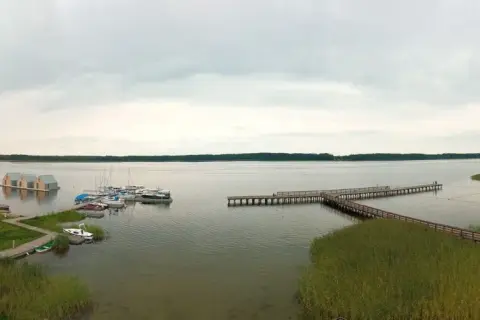 Widok na jezioro, gdzie wypływa roś. Widać pomosty, łodzie, pływające domki i plażę.