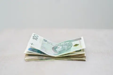 Stos polskich banknotów, w tym 100 zł, leży na jasnym tle. Zastanawiamy się, ile RMF zarabia na loterii.