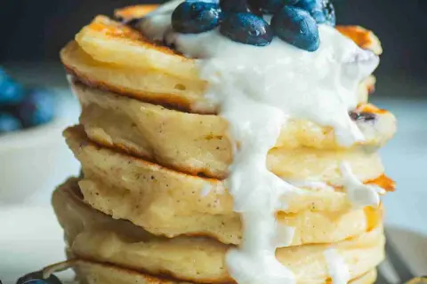 Ein Stapel fluffiger Protein Pancakes mit Blaubeeren und Joghurt. Perfekt für ein gesundes Frühstück, inspiriert von einem protein pancakes rezept.