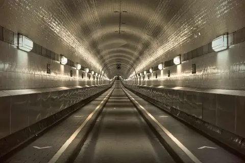 Der lange, beleuchtete Gang des alten Elbtunnels mit seinen gekachelten Wänden und Lichtern, die eine Perspektive erzeugen.