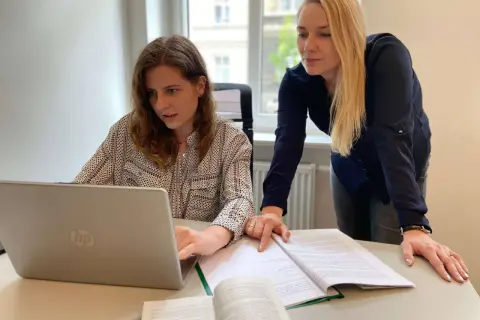Dwie kobiety pracują nad dokumentami i laptopem, przygotowując wniosek o rozwód online.