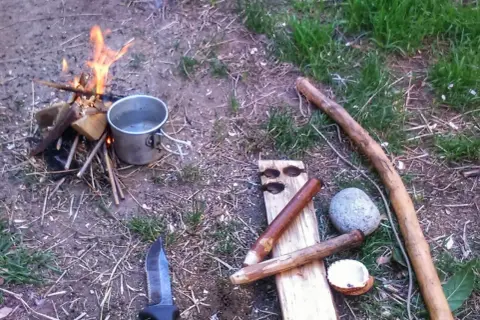 Un cuchillo, un cazo y leña para prender fuego. Preparativos para una noche al aire libre.