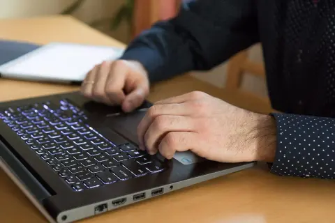 Dłonie pracują na laptopie z podświetlaną klawiaturą. Procesor AMD Ryzen 5 5600H zapewnia płynność pracy.