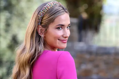 Joven sonriente con un peinado juvenil para boda, luciendo una diadema de pedrería y un vestido fucsia.