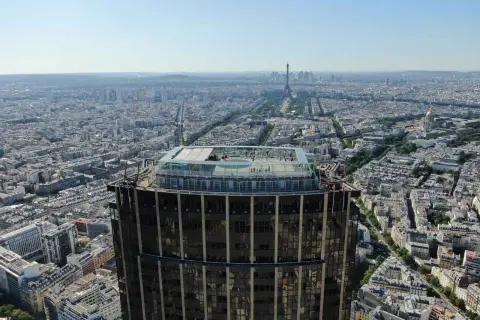 Vue aérienne de la **Tour Montparnasse** avec sa terrasse panoramique. Paris s'étend à perte de vue, avec la Tour Eiffel au loin.