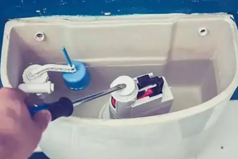 Mano con cacciavite che regola il meccanismo interno di uno scarico del water.