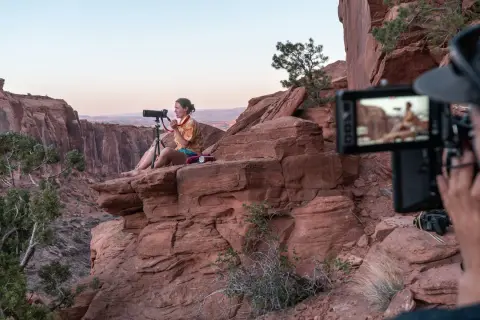 Krystle Wright, fotografa, siede su una roccia rossa in un canyon, mentre un operatore riprende la scena.