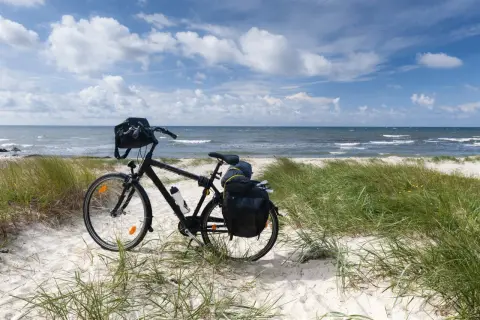 Rower z sakwami na plaży, gotowy do podróży trasą rowerową R10. Morze i niebo w tle.