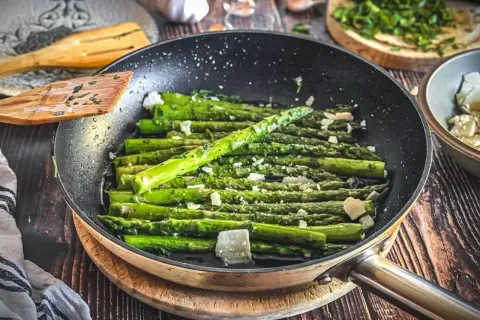Grüner Spargel wird in einer Pfanne mit Käse und Kräutern zubereitet. Ein köstliches Gericht, das zu vielen Spargel Rezepten passt.