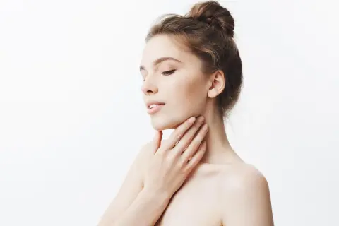 Delikatna skóra szyi, jak po zabiegu z kwasem glikolowym czy salicylowym. Kobieta dotyka swojej gładkiej szyi.