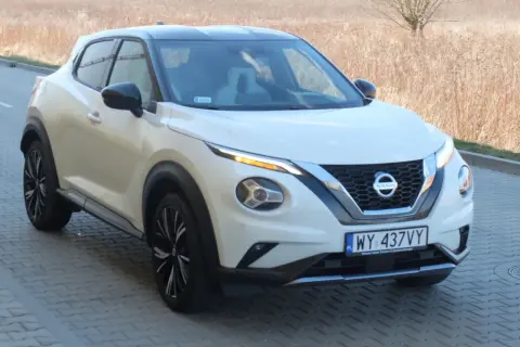 Biały Nissan Juke Sport z czarnym dachem i felgami, zaparkowany na kostce brukowej przy suchej trawie.