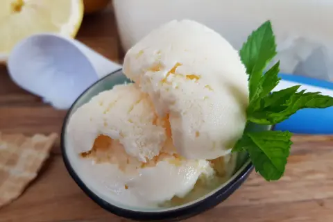 Erfrischendes zitroneneis mit joghurt, garniert mit Minze, daneben eine Waffel und Zitronenspalten.