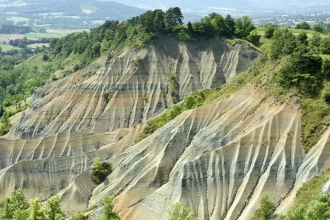 Le ravin de Corboeuf, un paysage spectaculaire aux strates colorées sculptées par l'érosion, dominé par une forêt verdoyante.