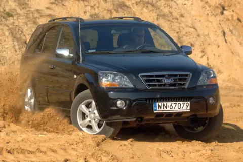 Czarny Kia Sorento 1. pokonuje piaszczysty teren, wzbijając tumany kurzu.