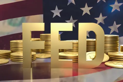 Złote litery "FED" na tle flagi USA i stosów monet. FOMC to komitet, który decyduje o polityce pieniężnej.