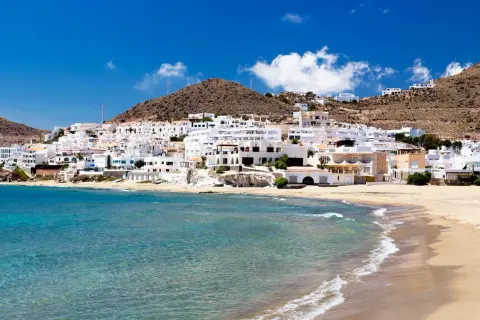 Costa blanca con aguas verde esmeralda, roquetas de mar, y casas blancas en la ladera.