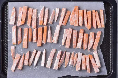 Pokrojone frytki z batatów posypane mąką na blasze do pieczenia.