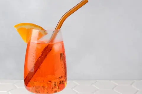 Ein Aperol Spritz mit Orangenscheibe und braunem Strohhalm auf Eis.