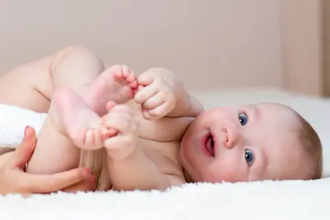 Uśmiechnięte dziecko z niebieskimi oczami, które właśnie wykonuje obroty z brzucha na plecy, bawiąc się swoimi stopami.