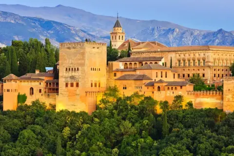 Alhambra, jeden z najpiękniejszych zabytków w hiszpańskich miastach, wznosi się na wzgórzu otoczony zielenią, z górami w tle.