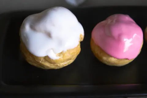 Deux petits choux garnis, l'un d'un glacage sucre glace blanc, l'autre d'un glacage rose.