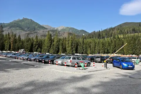 Parking Morskie Oko, cena za postój. Rząd samochodów na kamienistym parkingu, w tle las i góry.