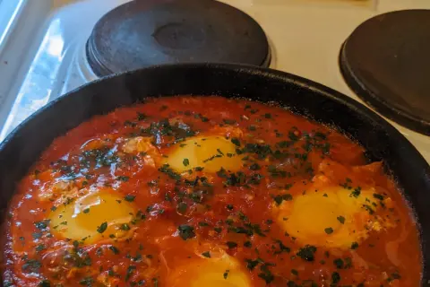 En varm och bubblande shakshuka med ägg i tomatsås, perfekt för ett mysigt frukostrecept.