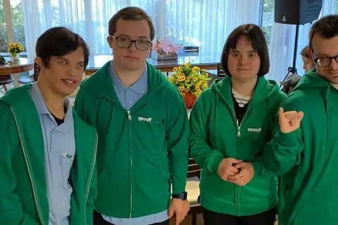 Quattro ragazzi con sindrome di Down, vestiti con felpe verdi, sorridono e posano per una foto.