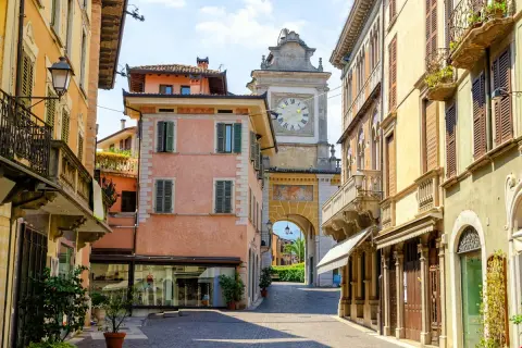 Un vicolo nel salò centro storico, con palazzi color pastello e un arco con orologio che conduce verso il lago.